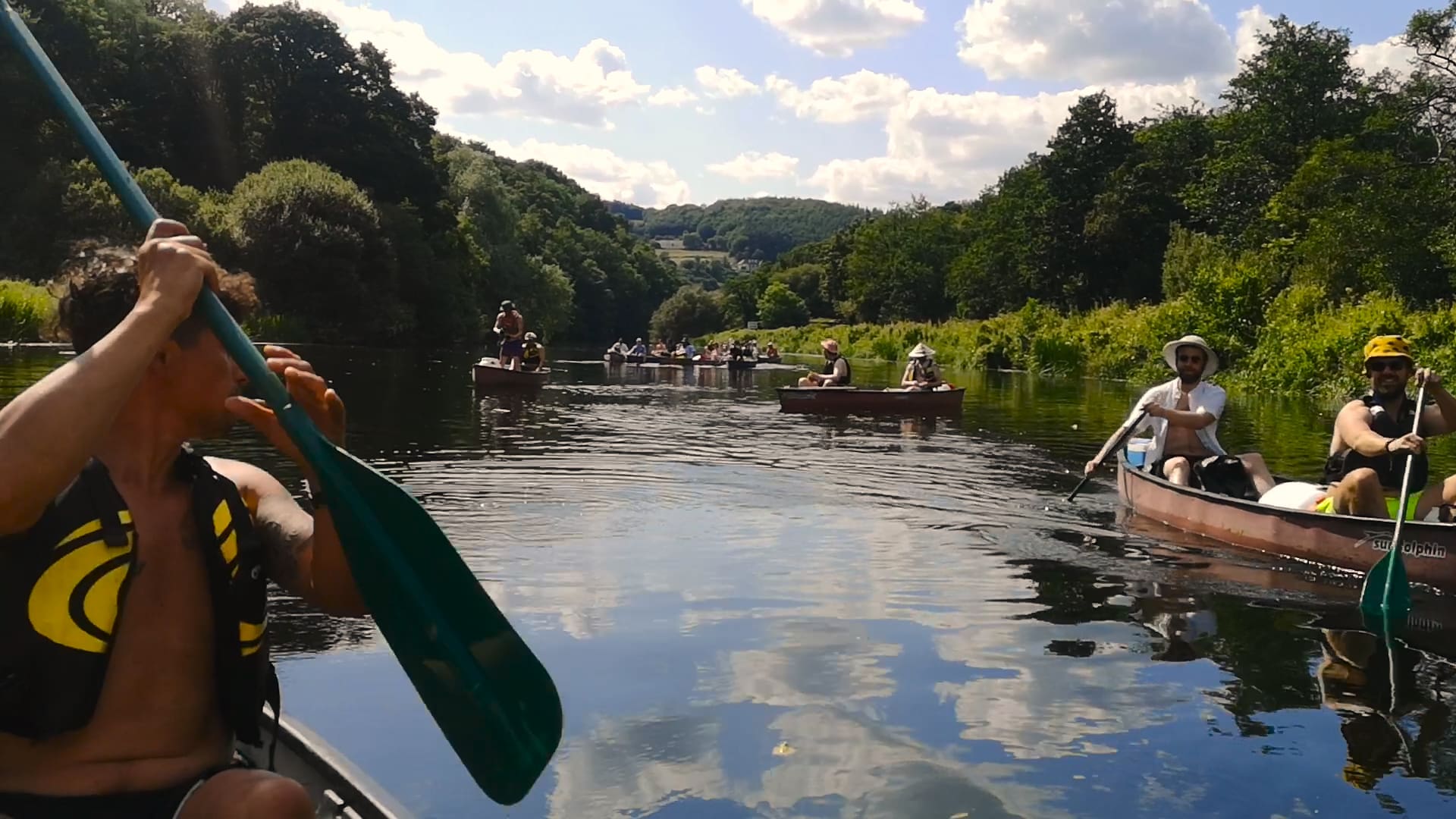 People paddle canoes on Irish river, surrounded by trees and hills in the background.