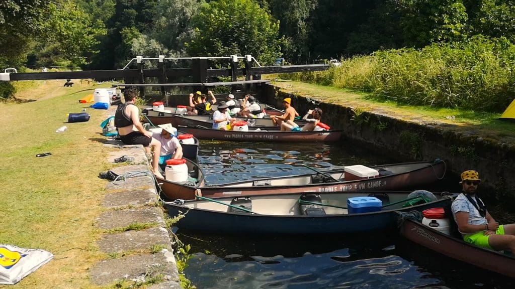 A group of people in 'Paddle Your Own Canoe' canoes. on a canal, surrounded by lush greenery.