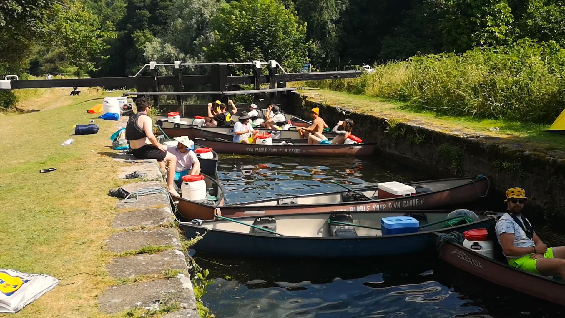 A group of people in 'Paddle Your Own Canoe' canoes. on a canal, surrounded by lush greenery.